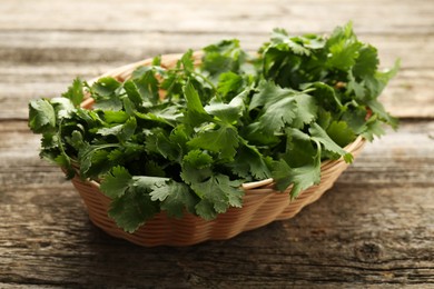 Fresh coriander in wicker basket on wooden table, closeup