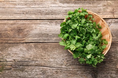 Fresh coriander in wicker basket on wooden table, top view. Space for text