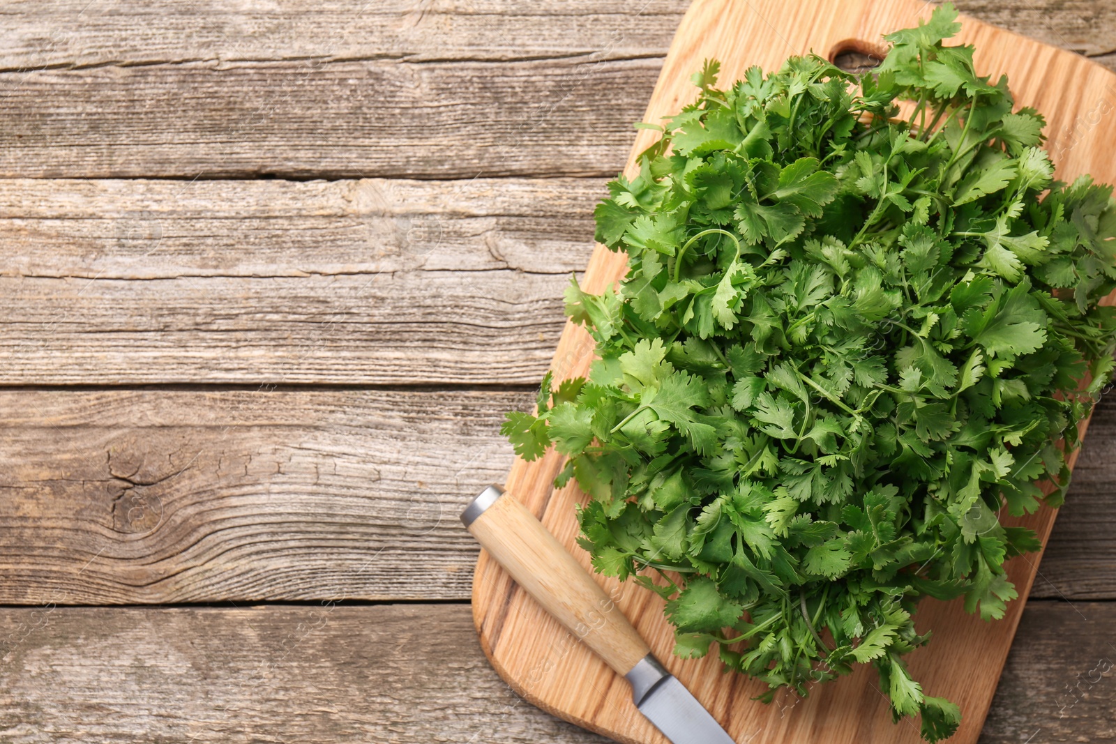 Photo of Fresh coriander and knife on wooden table, top view. Space for text