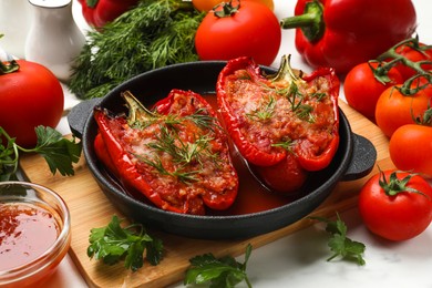 Photo of Tasty stuffed peppers in dish and ingredients on white table