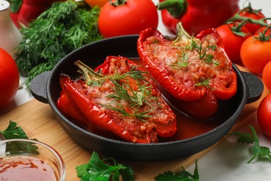 Photo of Tasty stuffed peppers in dish and ingredients on white table