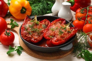 Photo of Tasty stuffed peppers in dish and ingredients on white wooden table