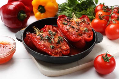 Photo of Tasty stuffed peppers in dish and ingredients on white tiled table