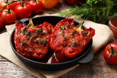 Photo of Tasty stuffed peppers in dish and ingredients on wooden table