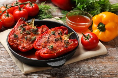 Photo of Tasty stuffed peppers in dish and ingredients on wooden table