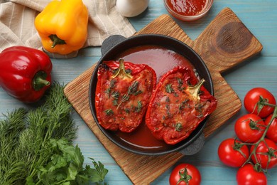 Photo of Tasty stuffed peppers in dish and ingredients on light blue wooden table, flat lay