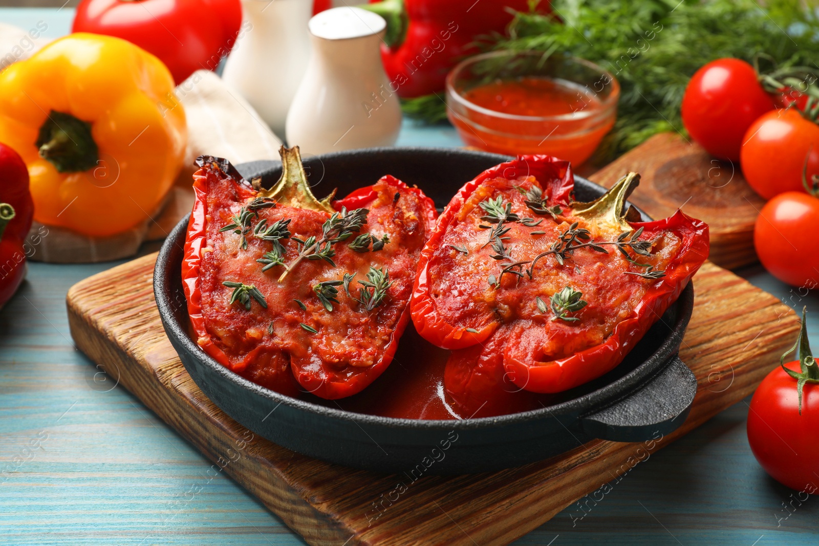 Photo of Tasty stuffed peppers in dish and ingredients on light blue wooden table, closeup