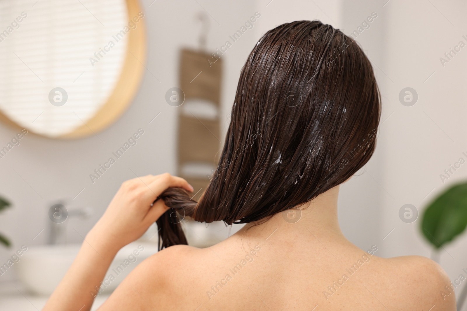 Photo of Woman applying hair mask in bathroom, back view