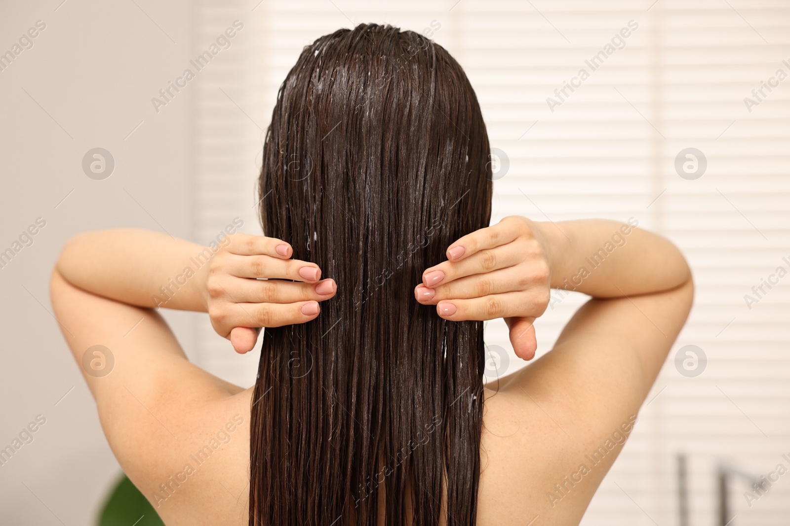 Photo of Woman applying hair mask in bathroom, back view