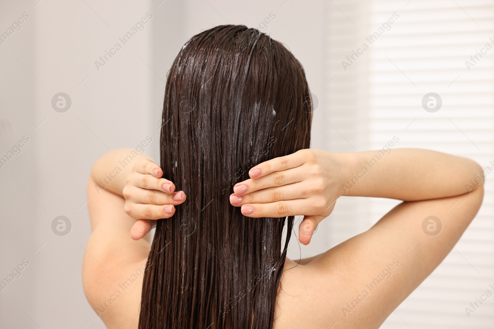 Photo of Woman applying hair mask in bathroom, back view