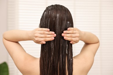 Photo of Woman applying hair mask in bathroom, back view