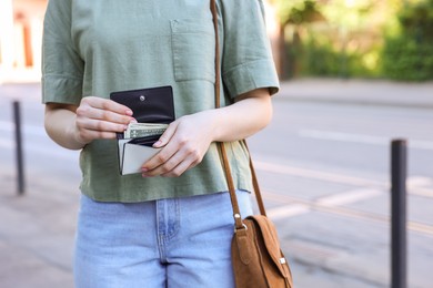 Woman holding purse with banknotes outdoors, closeup. Space for text