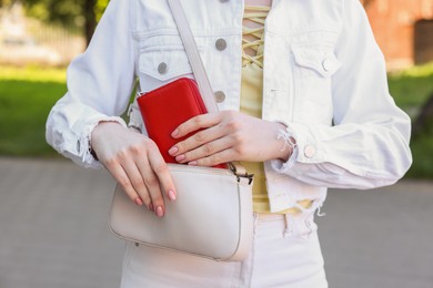 Woman putting purse into bag outdoors, closeup