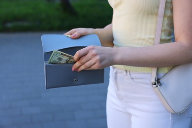 Photo of Woman holding purse with banknotes outdoors, closeup