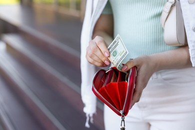 Woman holding purse with banknotes outdoors, closeup. Space for text