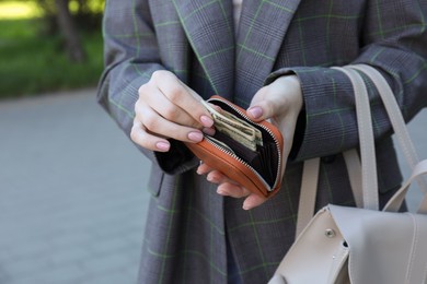 Photo of Woman holding purse with banknotes outdoors, closeup