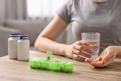 Photo of Woman with pills, organizer and glass of water at wooden table, closeup