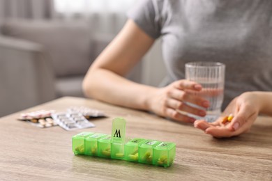 Photo of Woman with pills, organizer and glass of water at wooden table, closeup