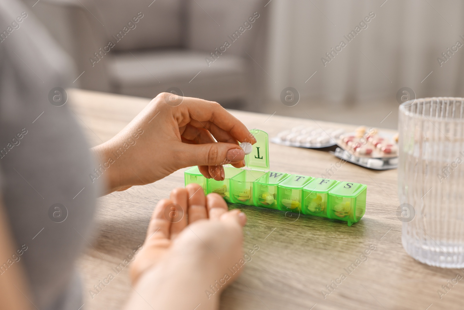 Photo of Woman with pills, organizer and glass of water at wooden table, closeup