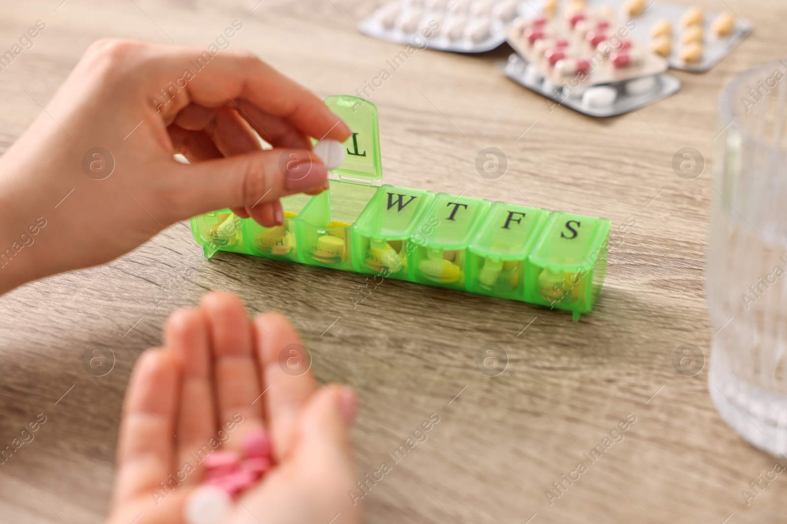 Photo of Woman with pills, organizer and glass of water at wooden table, closeup