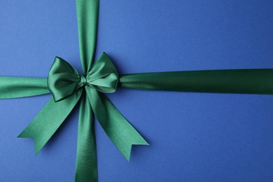Photo of Green satin ribbon with bow on blue background, top view