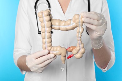 Photo of Doctor with model of large intestine on light blue background, closeup
