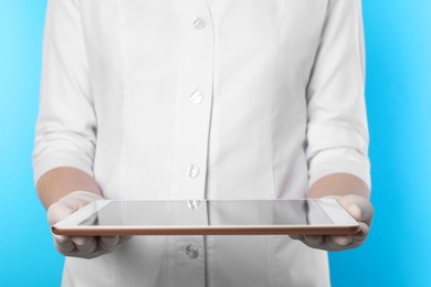 Photo of Doctor with tablet on light blue background, closeup