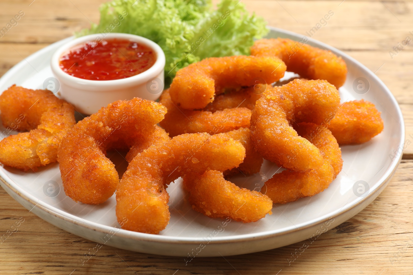 Photo of Tasty breaded fried shrimps served with sauce on wooden table, closeup