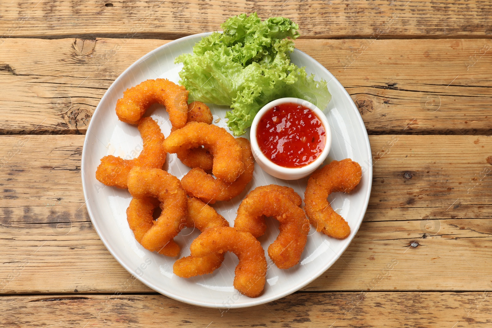 Photo of Tasty breaded fried shrimps served with sauce on wooden table, top view