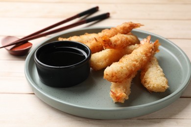 Tasty breaded fried shrimps served with sauce on light wooden table, closeup