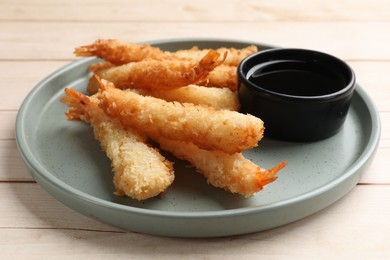 Photo of Tasty breaded fried shrimps served with sauce on light wooden table, closeup