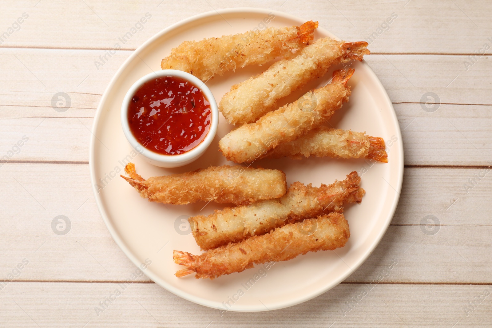 Photo of Tasty breaded fried shrimps served with sauce on light wooden table, top view