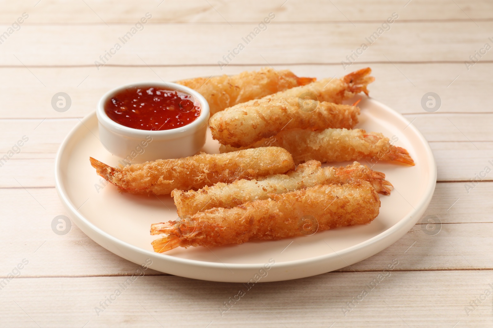 Photo of Tasty breaded fried shrimps served with sauce on light wooden table