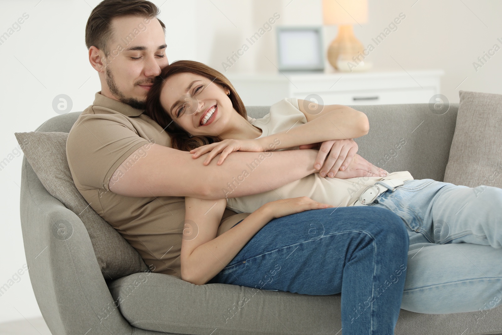 Photo of Man hugging his happy girlfriend on sofa at home