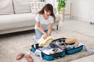 Woman packing suitcase for trip on floor indoors