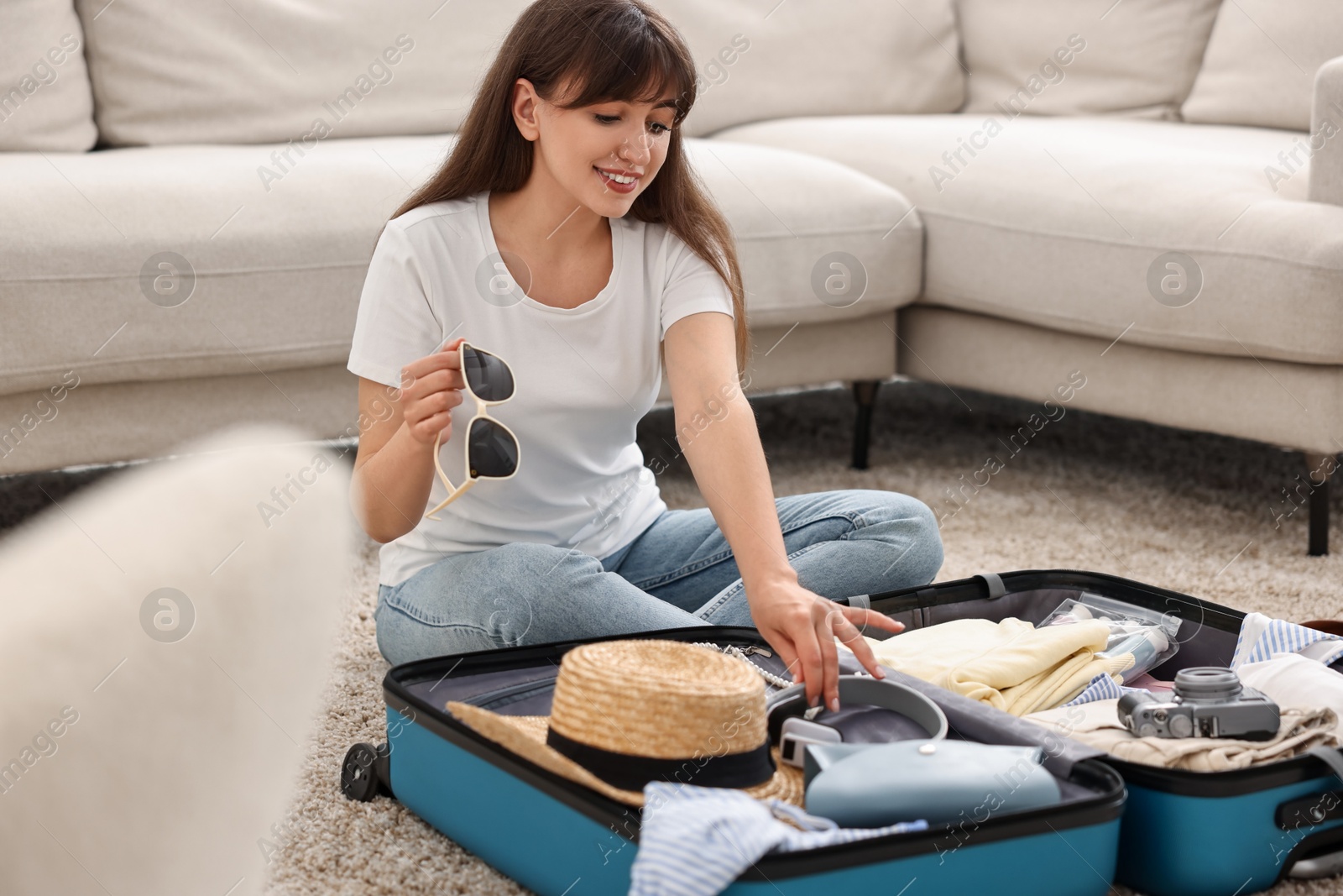 Photo of Woman packing suitcase for trip on floor indoors