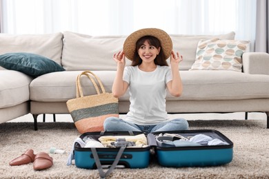 Woman packing suitcase for trip on floor indoors