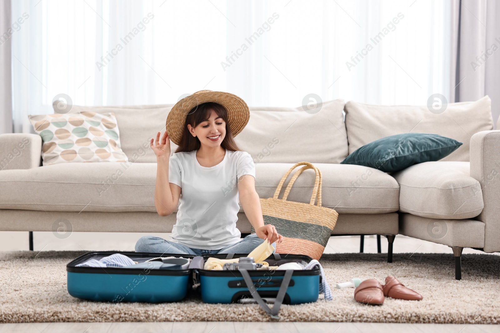 Photo of Woman packing suitcase for trip on floor indoors