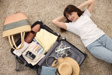 Woman packing suitcase for trip on floor indoors, top view