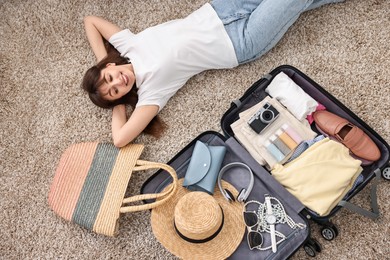 Photo of Woman packing suitcase for trip on floor indoors, top view