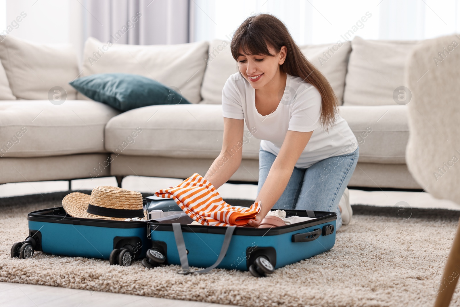 Photo of Woman packing suitcase for trip on floor indoors