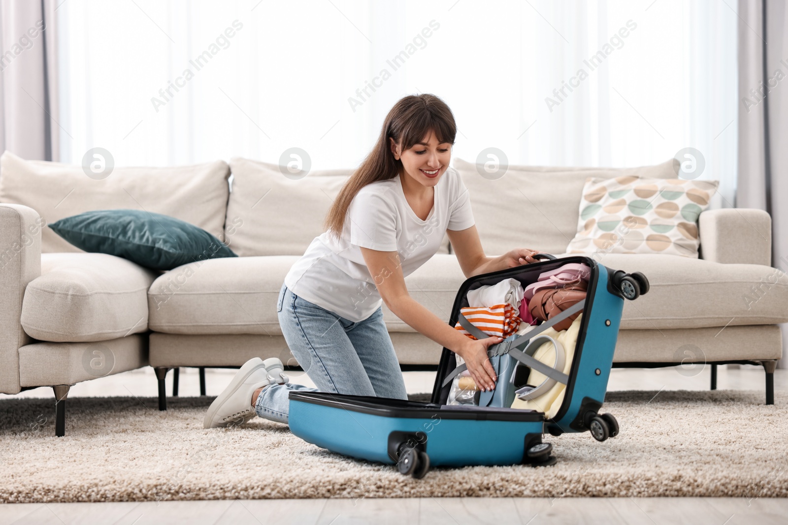 Photo of Woman packing suitcase for trip on floor indoors