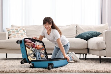 Photo of Woman packing suitcase for trip on floor indoors
