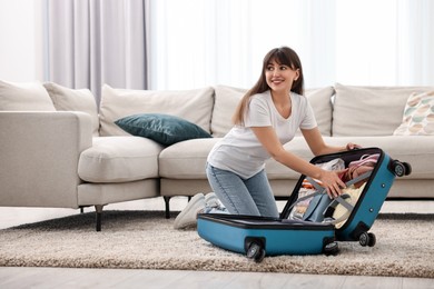 Woman packing suitcase for trip on floor indoors