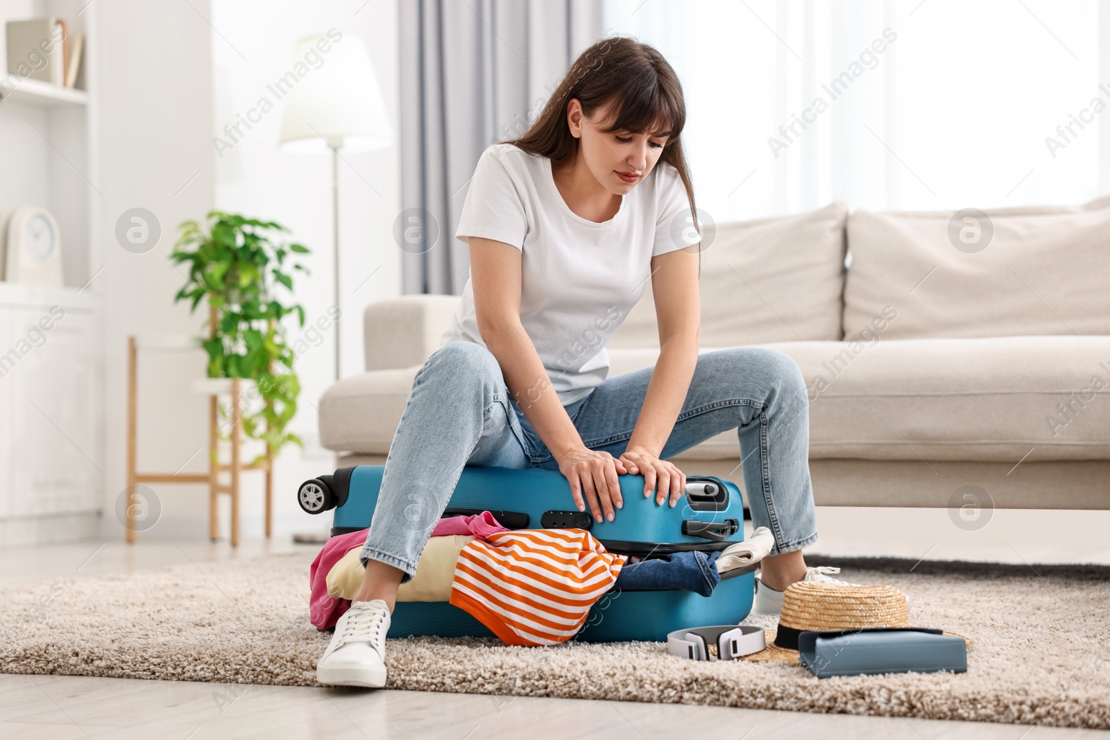 Photo of Woman packing suitcase for trip on floor indoors