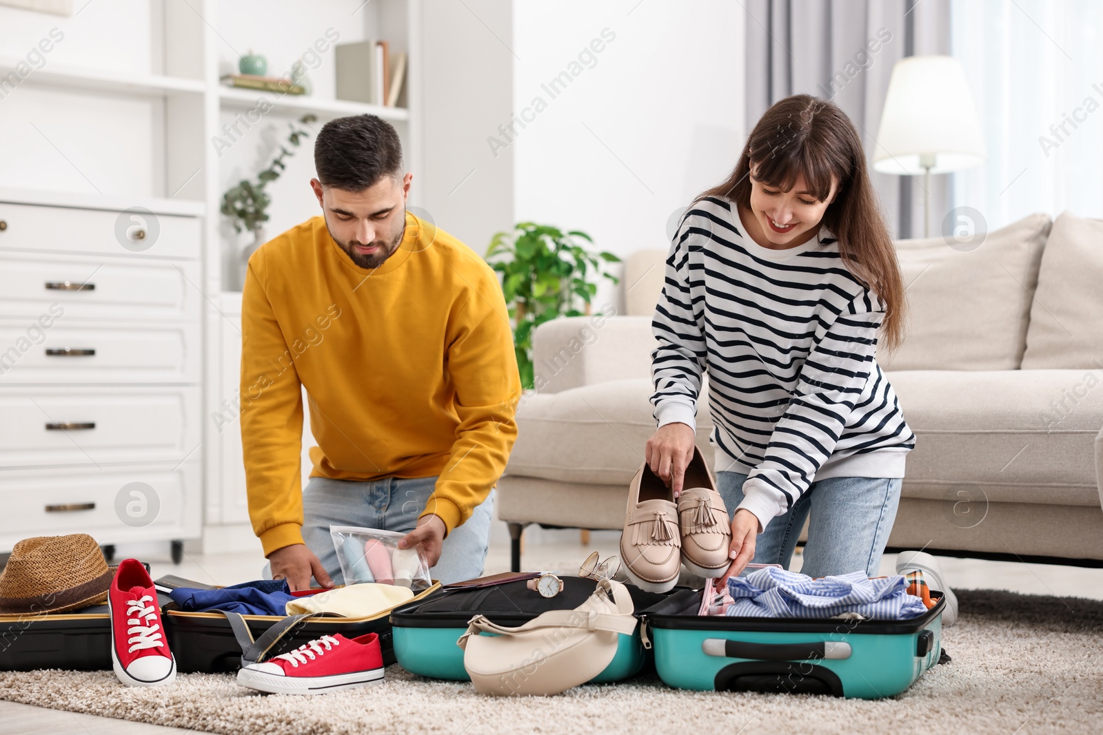 Photo of Couple packing suitcases for trip on floor at home