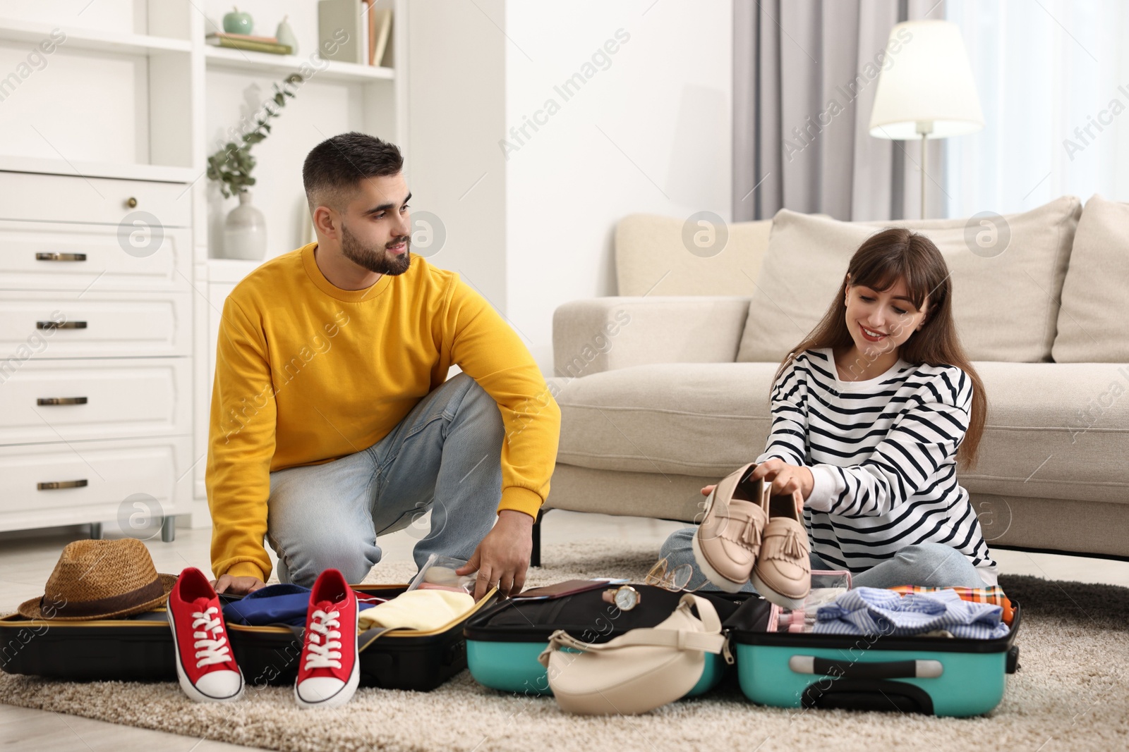 Photo of Couple packing suitcases for trip on floor at home