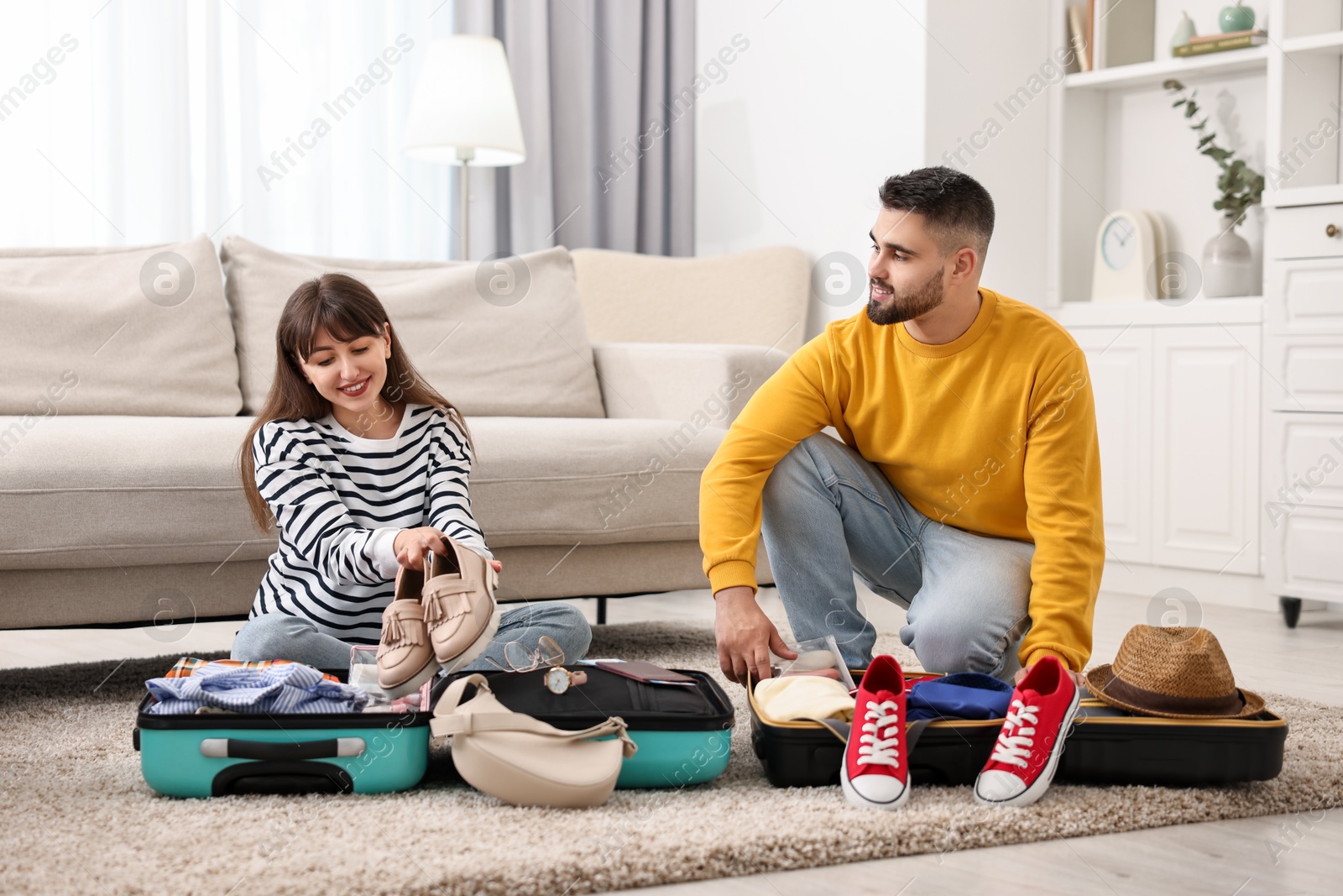 Photo of Couple packing suitcases for trip on floor at home