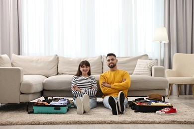 Photo of Couple near suitcases with clothes on floor indoors