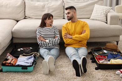 Couple near suitcases with clothes on floor indoors